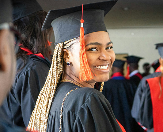 A graduating student in cap and gown smiling at a commencement ceremony